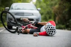 Cykelrytter væltet på vejen, der ligger foran en bil.